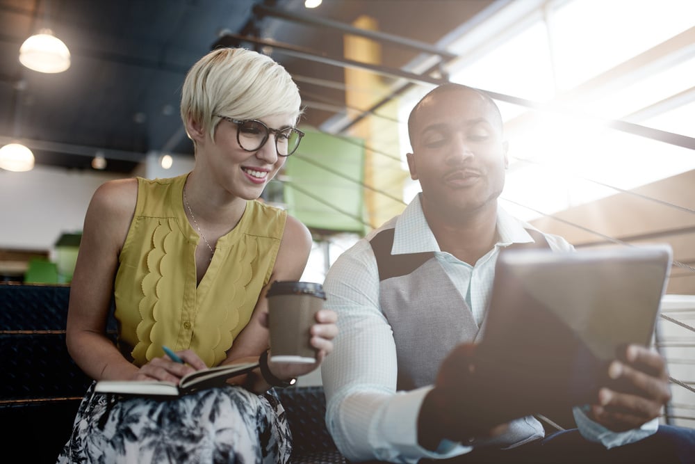 Two creative millenial small business owners working on social media strategy using a digital tablet while sitting in staircase Two creative millenial small business owners working on social media strategy using a digital tablet while sitting in staircase